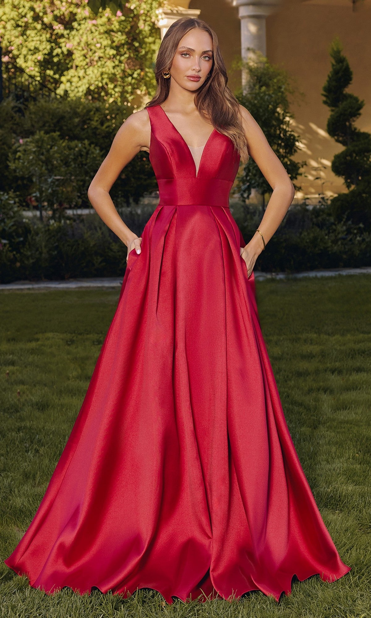 A woman stands outdoors wearing the Amoris T814 long prom dress in burgundy, featuring a sleeveless, floor-length A-line silhouette with a deep V-neckline and side pockets.